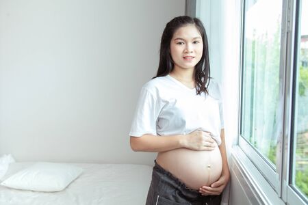 Happy thai pregnant woman with big tummy relax at home. Portrait of pregnant mature woman standing...