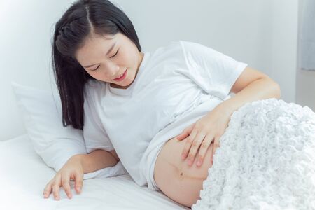 The pregnant woman is petting and looking at her stomach.