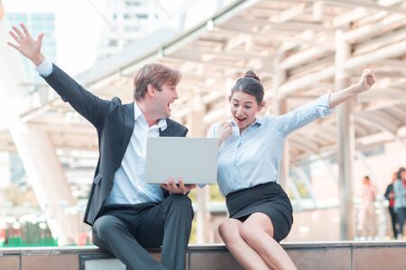 Celebrating success.Excited cheerful young business couple keeping arms raised and expressing positivity as they know the success of their laptops.の写真素材