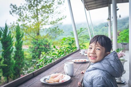 Smiling Asian boy is eating breakfast on a beautiful natural background detailの写真素材