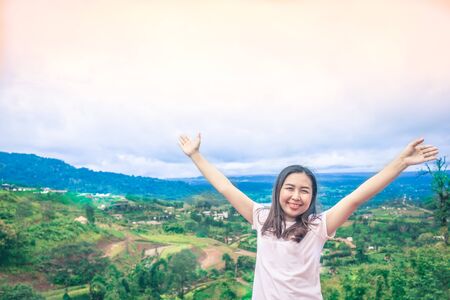Happy Asian woman stands her arms on a beautiful view of the mountains and the sky detail natureの写真素材