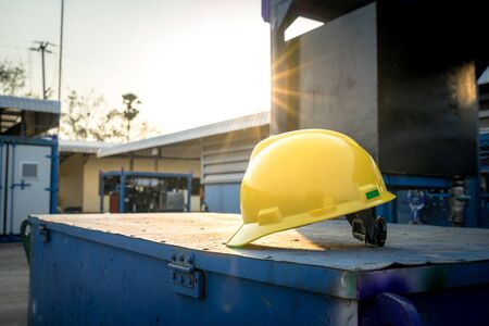 Yellow hardhat or safety helmet for technician worker is placed on toolbox at workshop yard with sun...