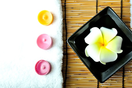 A plumeria in the plate and three candles with white towel on bamboo mat. の写真素材