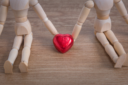 A couple of wooden doll man on valentine days showing love to each other and focus either on heart-shaped chocolate and the coupleの写真素材
