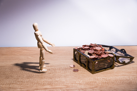 A wooden doll man with his savings, gold coin. All composed with thai baht twenty-five cent, fifty cent, thai baht and yuanの写真素材