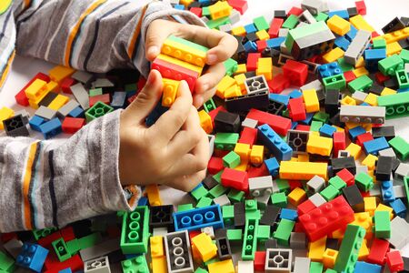 Child's hand building plastic toy blocks with blurred background.