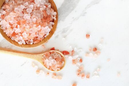 top view of himalayan pink rock salt in wooden bowl and spoon on white marble table.