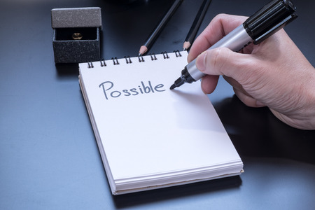 "Possible" is written on small notepad with a board marker, pencil and giftbox on PVC blackの写真素材