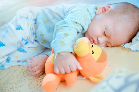 Sleeping baby in bed  holding doll.の写真素材