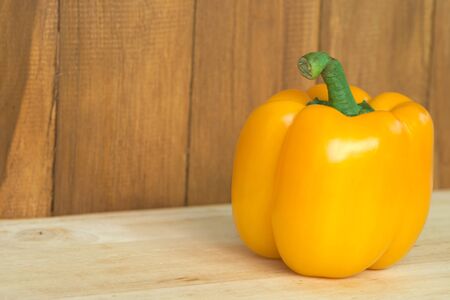 Single yellow bell pepper over wooden table and brown wooden background