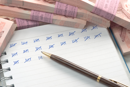 Abstract pile of money on top of ring bound book with mark showing amount of counted moneyの写真素材