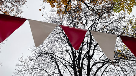 Red and white triangular bunting hanging against a background of bright yellow autumn foliage and skyの写真素材