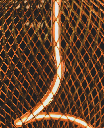 Close-up of a warm glowing LED filament light bulb inside a diamond metal mesh cageの写真素材