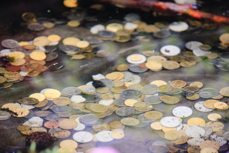 Scattered coins of various colors lying at the bottom of a shallow fountain or wishing wellの写真素材