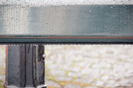 Close up of a smooth, gray metal railing covered in fresh rain drops with a blurred orange backgroundの写真素材