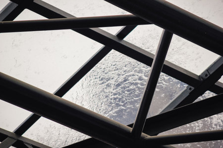 Rain falling on a transparent glass roof with water dripping from the dark metal support structure belowの写真素材