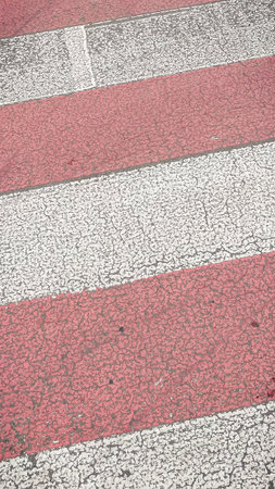 Close-up texture of a worn red and white zebra pedestrian crossing on a cracked asphalt roadの写真素材