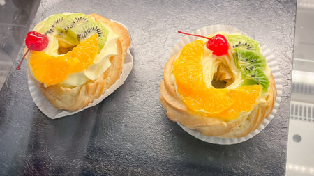 Two delicious choux pastry rings filled with cream and topped with fresh kiwi, orange, and cherry.の写真素材