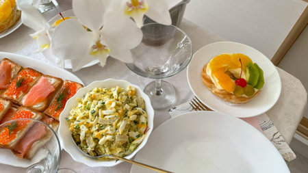 Festive table with fruit pastry, salmon sandwiches, egg salad and elegant setting for celebration.