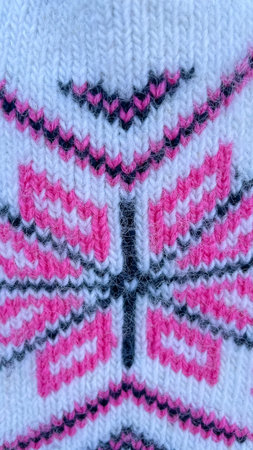 Macro shot of a pink and white knitted wool ornament with a traditional folk pattern for winter...