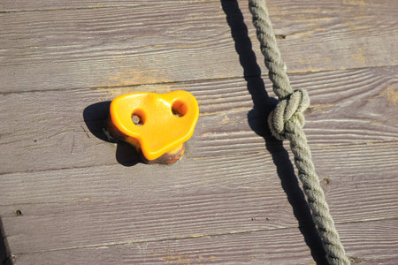 Close-up of a yellow climbing hold and a thick knotted rope on a weathered wooden wall at an outdoor playground.の写真素材