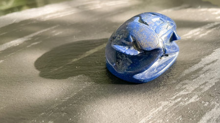 Ancient style blue scarab beetle carved from stone on a dark textured background. Egyptian souvenir.