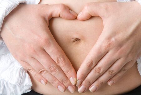 The pregnant woman make heart from fingers. 