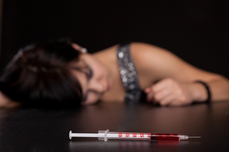 Drug addict woman with syringe is syringe is sleeping on table. Simulated, studio shotの写真素材