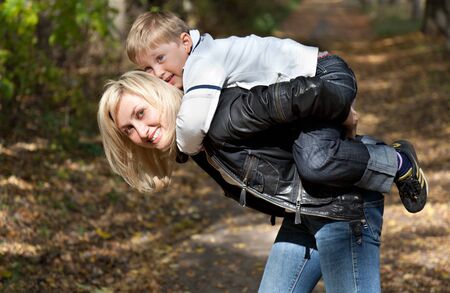 a smiling woman is holding her son on her backの写真素材