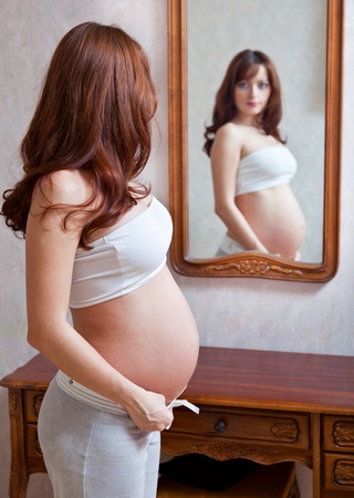 a beautiful pregnant woman is looking at herself in the mirrorの写真素材