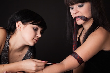 a beautiful girl is stabing to her girlfriend a drug (imitation)の写真素材