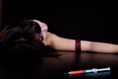 Drug addict woman with syringe is sleeping on table. Simulated, studio shotの写真素材