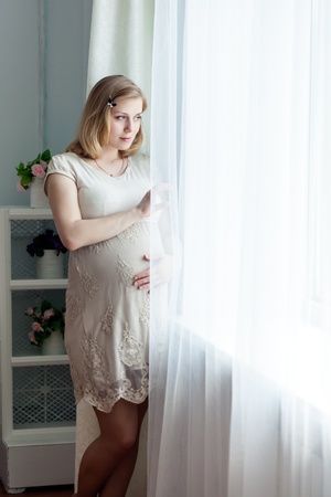 Pregnant woman is standing near the windowの写真素材