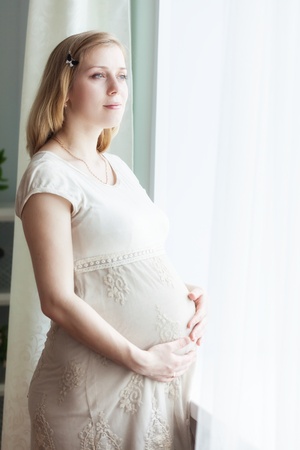 Pregnant woman is standing near the windowの写真素材