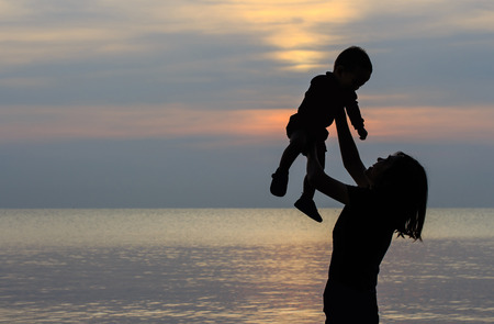 Silhouette of mother and her little son on the beach at sunriseの写真素材