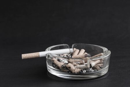Many cigarette stubs and ash in a glass ashtray on black background