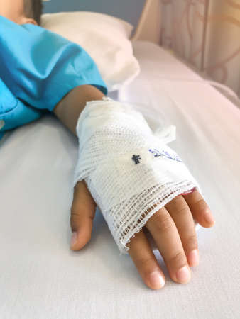 Close-up of a pediatric patient's hand with a gauze wrap needle for intravenous fluid administration.の写真素材