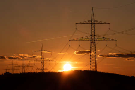 Electricity pylons in the evening sun. Some clouds in the sky.
