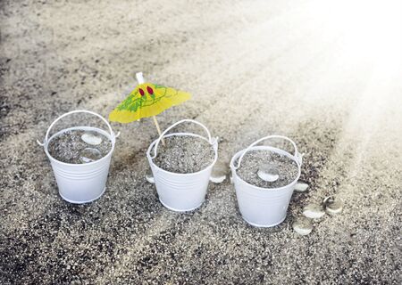 Little white buckets full of sand on the sandy beach. Summer holiday concept background, travel themes with cocktail umbrellaの写真素材