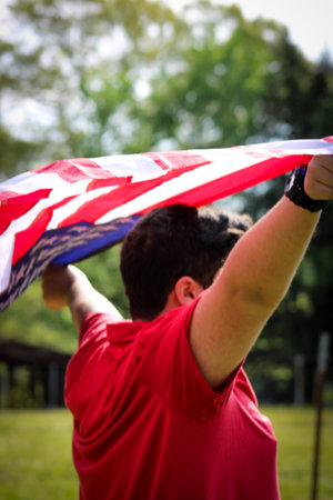 Young man in field holding American flag blowing in the wind.の写真素材