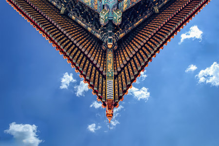 Upward view of ornate Forbidden City roof eaves against bright blue sky, showingcasing traditional...