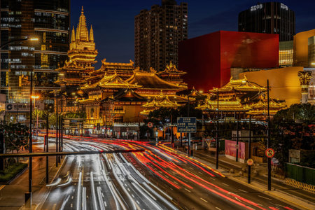 A stunning night photo of Shanghai's Jing'an Temple, illuminated in golden light, with vibrant car...