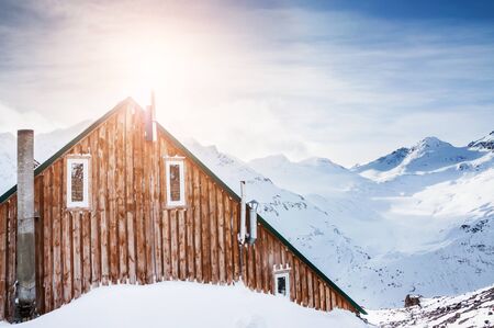 Wooden house in the mountains. Beautiful winter landscape with snow-covered mountains at sunsetの写真素材