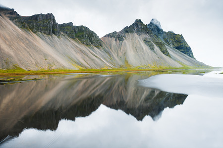 Mountains and reflections on the coast of Atlantic ocean. East Icelandの写真素材