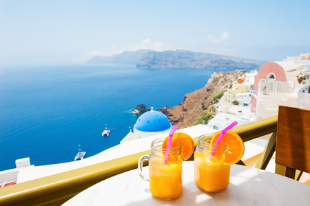 Beautiful view of Santorini island, Greece. Two glasses of fresh orange juice on the table.の写真素材