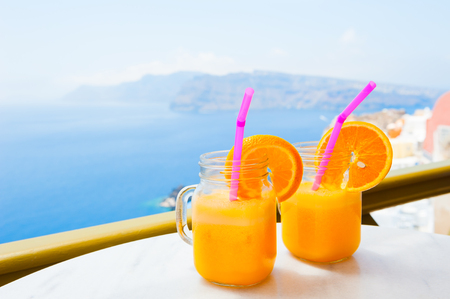 Two glasses of fresh orange juice on the table. Beautiful view of Santorini island, Greece.の写真素材