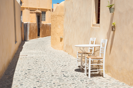 Table with two chairs on the cozy street in Santorini island, Greece.の写真素材