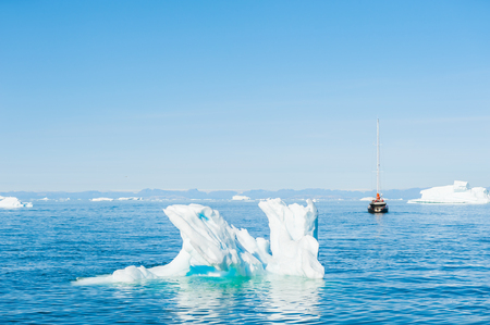 Yacht sailing among icebergs in the Atlantic ocean in Greenlandの写真素材