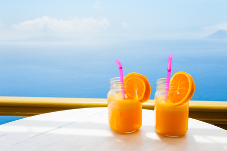 Two glasses of fresh orange juice on the table overlooking the sea.の写真素材