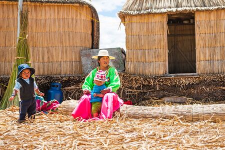 Titicaca lake, Puno, Peru - March, 20, 2017: Woman in traditional dresses with children on Uros floating islands on Titicaca lake in Puno, Peru, South Americaのeditorial素材